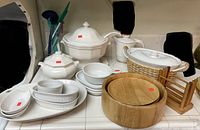 Photo showing white ceramic casserole dishes, bowls, ramekins, wooden bowls, and a wooden rack arranged on a counter.