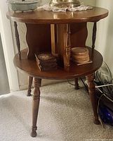 Photo of vintage oak round side table with a lower shelf and turned legs, with wooden coasters and decorative items placed on the lower shelf.