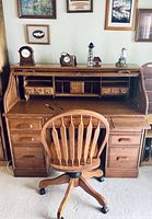 Front view of the oak roll top desk open showing interior compartments and matching oak swivel chair in front