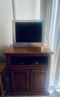 Oak wooden side table with a lower cabinet and open shelf, supporting a silver Sharp CRT TV and a small box on top.