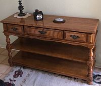 Oak sofa table made of oak wood with brass handles on drawers, two lower shelves, and turned legs. Minimal wear visible.
