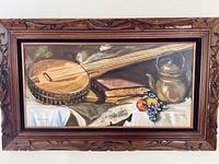 Frontal view of the oil painting showing the banjo, books, jug, fruit, and surrounding elements within a carved wooden frame.