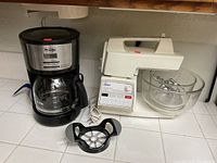 Photo showing Mr. Coffee drip coffee maker next to Oster mixer system with glass bowl and mixer attachments on kitchen counter.
