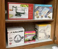 Photo of boxed apple peeler, tart sealer set, Kalorik egg cooker, Magic Roller Slicer, and OXO food grinder on shelf