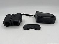 Front view of Argus 7x25 binoculars with attached neck strap, soft carrying case, and removable eye shield.