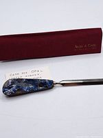 Letter opener with opal handle and blade alongside a maroon cloth case with Angus & Cook branding, on a white background.