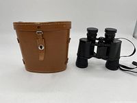 Brown leather carrying case with stitched edges and snap button on front. Shows some use consistent with vintage item. Positioned beside binoculars.