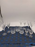 Full view of the 10 pieces of crystal glassware arranged on cloth background showing wine glasses, tumblers, and cocktail glasses.