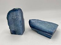 Pair of blue geode bookends shown on a white background. One standing upright, the other lying down, showing crystal interior and banded polished exterior.
