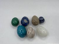 Full view of seven decorative stone eggs arranged on a white surface showing variety of color and size.
