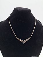 Front view of the sterling silver necklace displayed on a black velvet bust showing the V-shaped geometric pendant and fine chain.