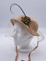 Side profile of beige vintage hat showing veil, floral arrangement, and long black feathers.