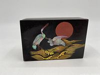 Top view of rectangular black lacquered wooden box, showing two cranes in iridescent paint, red circular sun, and gold stylized foliage or waves.