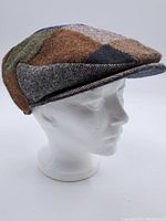 Side view of wool patchwork cap on a white mannequin head showing curved brim and patch designs