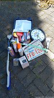 Overview of automotive goods lot showing Team TOYO wall clock, license plate, emergency roadside kit, window scrapers, car cleaning products, and various small automotive accessories scattered on pavement.