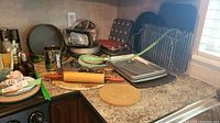 Overview photo showing various baking pans and racks spread on kitchen countertop including round pans, muffin tins, rolling pin, and cooling racks.