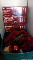 Three boxed sets of Fusion 3-piece holiday stake lights stacked with the holiday fabric tree skirt, red baubles, and Christmas beads in a bin