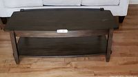 Front angled view of modern espresso colored coffee table with lower shelf in front of white couch on hardwood floor.