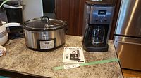 Photo showing both the coffee maker and Crockpot on kitchen counter with Cuisinart coffee maker manual visible.