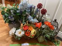 Full view of the silk floral arrangements grouped together showing various flowers and containers on wooden floor.