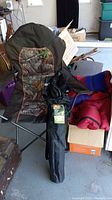 Photo of deluxe folding arm chairs with camouflage fabric, rolled sleeping bag and acrylic blankets on concrete floor indoors