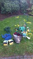 Overview of all garden items on grass showing hoses, metal plant supports, spray nozzles, garden edging, and various tools