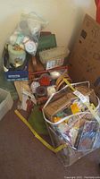 Photo showing a collection of baskets, boxes, and plastic bags filled with wool, yarn, sewing kits, and craft supplies clustered in a corner.