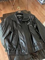 Image of black leather jacket with zip and button closures and collar, showing front and sleeve details.