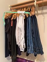 Various ladies pants hanging on wooden hangers on a rack, including white, black, and denim pants.