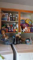 Wide view of cabinets and countertop showing numerous laundry and cleaning products from various brands, some stacked and grouped.