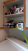 Cabinet shelf with multiple packaged light bulbs and loose bulbs, including green and red party bulbs and compact fluorescents.