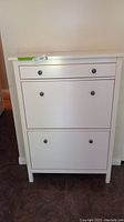 Front view of the white narrow cabinet showing three drawers with black round knobs.