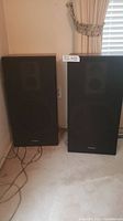 Two Technics speakers standing side by side with black fabric front grilles.
