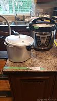 Side by side view of a vintage aluminum Presto pressure cooker and a modern Power electric pressure cooker on kitchen counter.