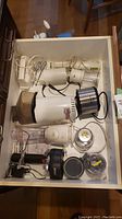Drawer filled with various small kitchen appliances including vintage popcorn maker, Braun hand blender and attachments, hand mixers, blender, potato peeler