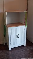 Front view of a small white cabinet with two doors and wood finish top.