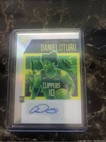 Front photo of Daniel Oturu Panini Prizm Flux Silver Holo rookie card showing player portrait, Clippers uniform, autograph in blue ink, and holographic design.