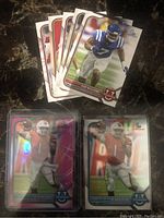 Photo showing a set of NFL rookie cards with standard and parallel designs, featuring players in football gear, some with holographic foil, on a dark surface