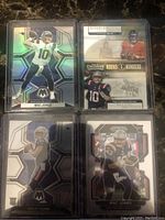 Four football rookie cards featuring Mac Jones, Justin Fields, and Bailey Zappe in protective sleeves, showing front sides with holographic and detailed images.