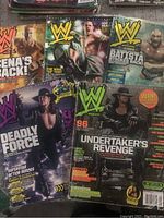 Photo showing WWE Magazines featuring The Undertaker, Batista, John Cena, and Triple H prominently on the covers with vibrant action shots and theme titles.