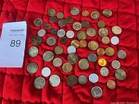 Photo showing 52 coins scattered on red cloth background with a MaxSold lot number card.