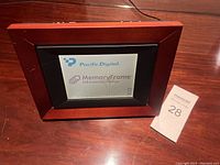 Wood-look framed digital photo frame placed on a wooden surface, screen displaying the Pacific Digital MemoryFrame branding.