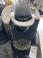 Photo of a black and silver Keurig coffee maker machine with visible water reservoir and drip tray.
