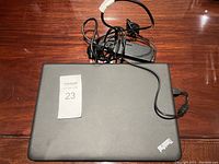 Closed Lenovo ThinkPad laptop on wooden surface with charger cable coiled beside it.