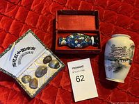 Photo shows a small white porcelain vase with Asian landscape, miniature fish-shaped ornament in a red box, and a package of polished decorative stones with Chinese writing.