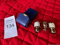 Binoculars beside a blue leather case on red quilted background