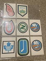 Front side of 8 hockey team logo cards featuring vibrant logos of Detroit Red Wings, Los Angeles Kings, Montreal Canadiens, New York Islanders (two cards), Toronto Maple Leafs, and Minnesota North Stars, arranged in a 3x3 grid with one slot empty.