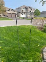 View of two black iron flower hangers standing upright in a lawn, showing the height and design.