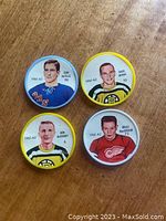 Four plastic hockey coins featuring players Bruce MacGregor (Detroit Red Wings), Doug Mohns (Boston Bruins), Jean Ratelle (New York Rangers), and Don McKenney (Boston Bruins) front sides with player photos and details.
