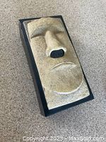 Front angled view of the Tiki tissue box holder with textured face and large nose on black base.